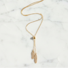 Gold necklace with feather pendants on a marble surface
