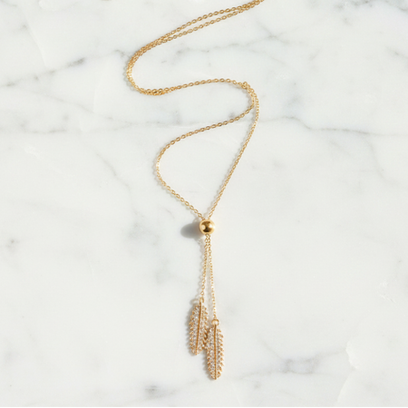 Gold necklace with feather pendants on a marble surface
