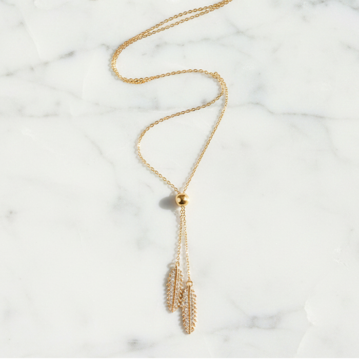 Gold necklace with feather pendants on a marble surface
