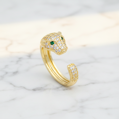 Gold snake-shaped ring with green eyes on a marble background
