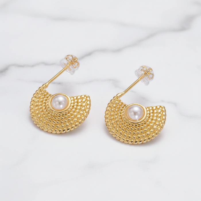 Gold earrings with pearl center on a white marble background