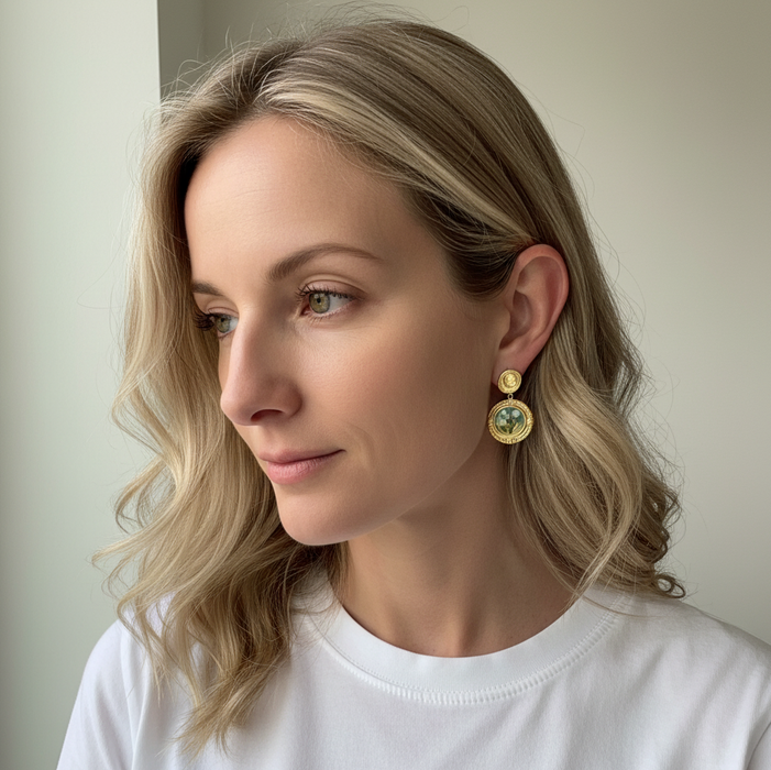 Woman wearing gold earrings with green gemstones against a neutral background
