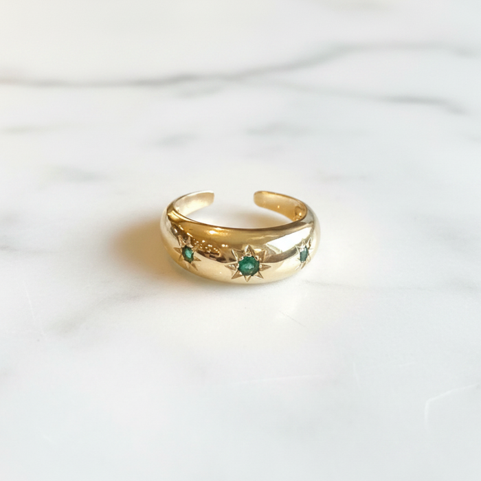 Gold ring with emerald stones on a white fabric background