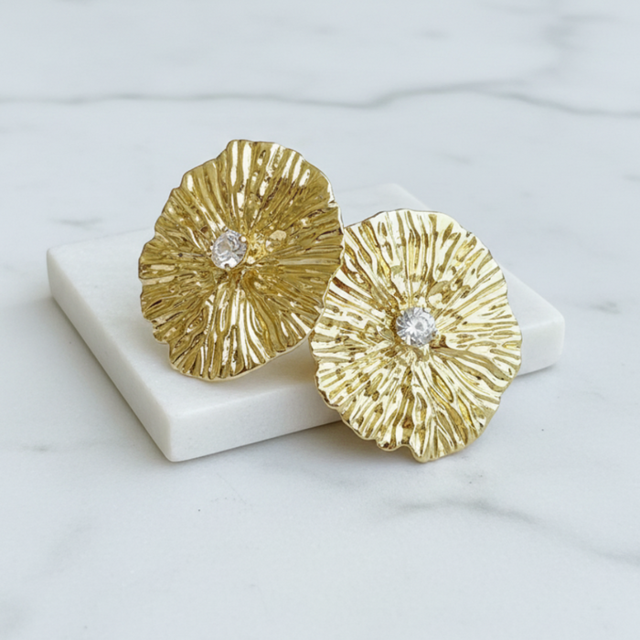 Gold floral earrings with embedded diamonds on a white stand against a light marble background