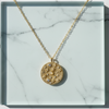 Gold necklace with a decorative pendant on a marble surface