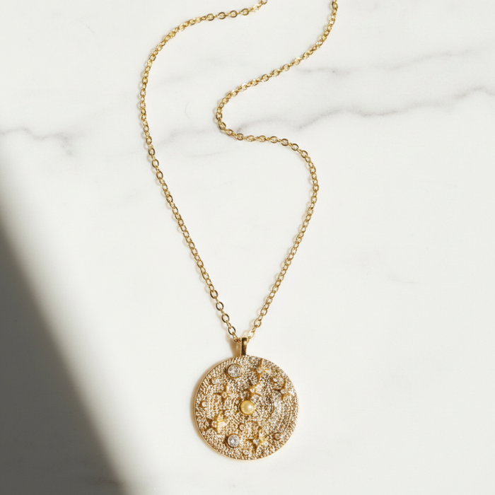 Gold necklace with a round, intricately designed pendant on a light background