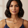 Woman wearing a gold necklace and navy blue top against a beige background
