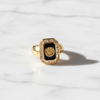 Gold ring with a black center and gemstones on a white marble background
