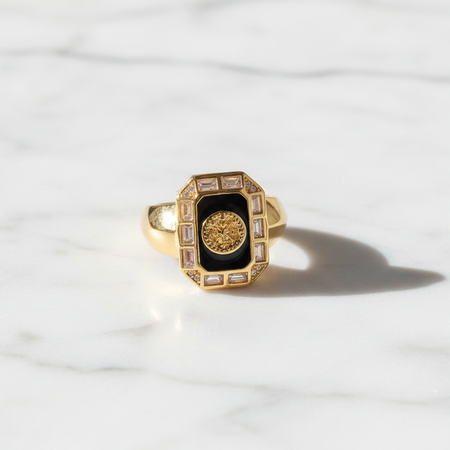 Gold ring with a black center and gemstones on a white marble background