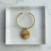 Gold bracelet with a round pendant in a clear box on a marble surface