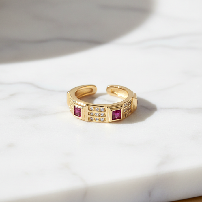 Gold ring with embedded red stones on a marble surface