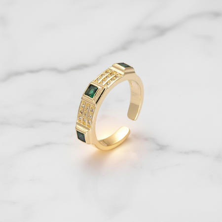 Gold ring with green gemstones on a light gray background