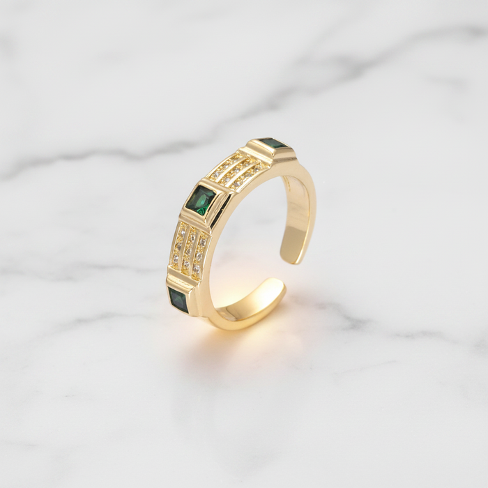 Gold ring with green gemstones on a light gray background