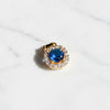 Gold pendant with a blue gemstone and diamond accents on a white background
