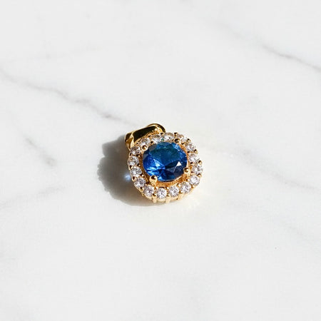Gold pendant with a blue gemstone and diamond accents on a white background