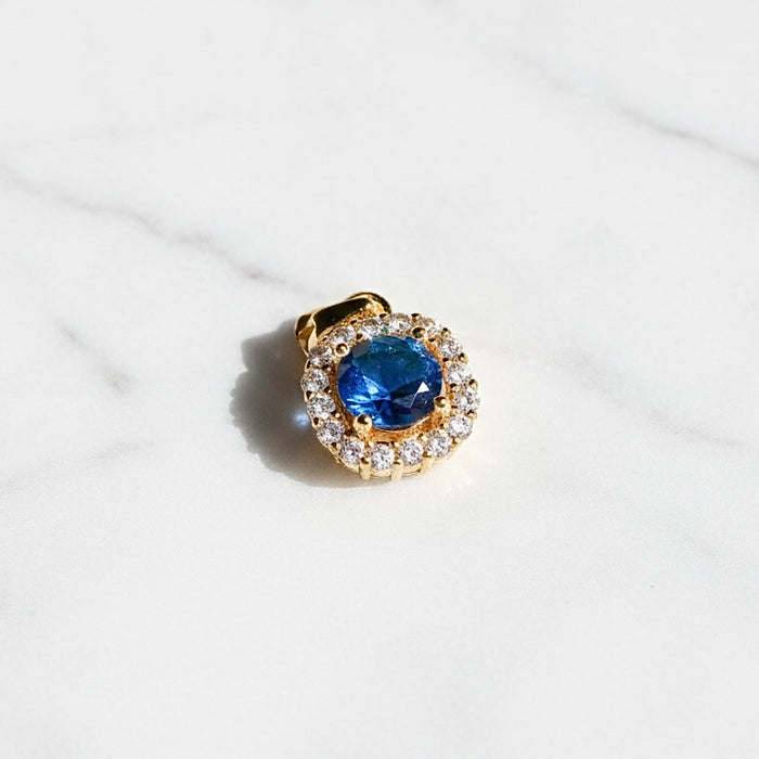 Gold pendant with a blue gemstone and diamond accents on a white background