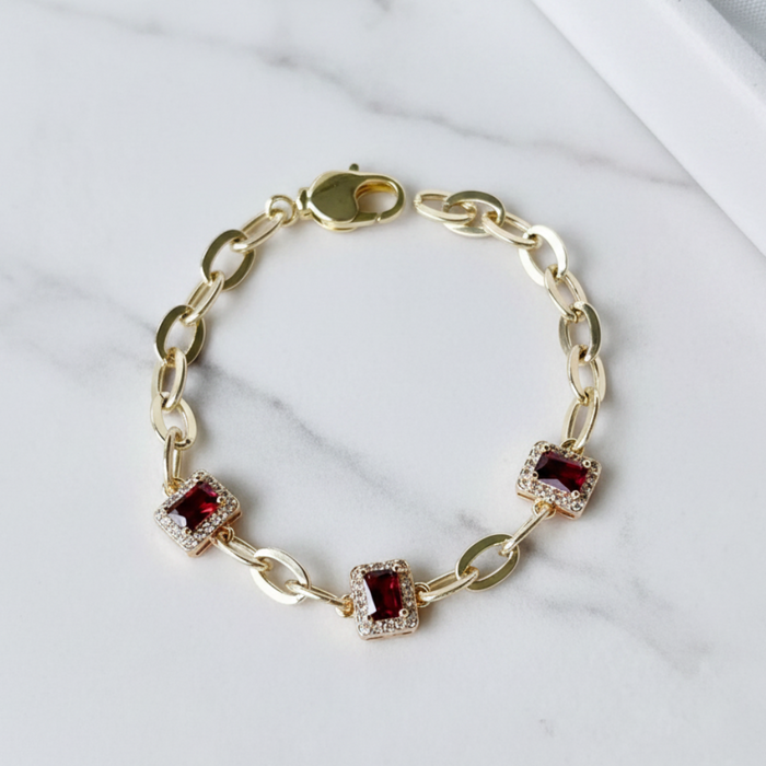 Gold bracelet with red gemstones on a marble surface