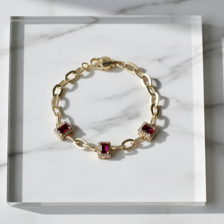 Gold bracelet with red gemstones on a marble surface