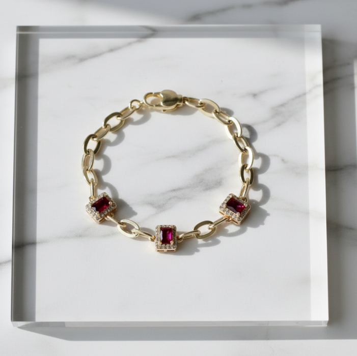 Gold bracelet with red gemstones on a marble surface