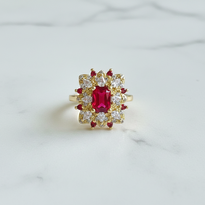 Gold ring with a red gemstone and diamond accents on a light gray background