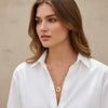 Woman wearing a white shirt and gold necklace with a beige background