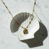Gold necklace with a blue gemstone pendant on a white shell against a marble background