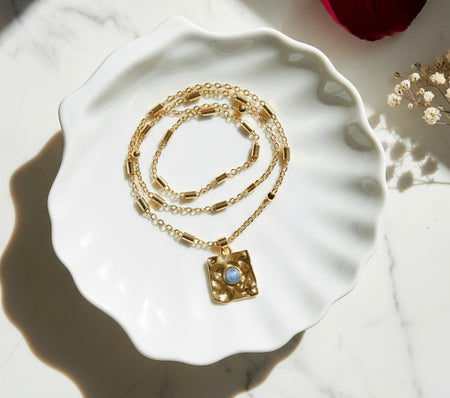 Gold necklace with a pendant on a white ceramic dish