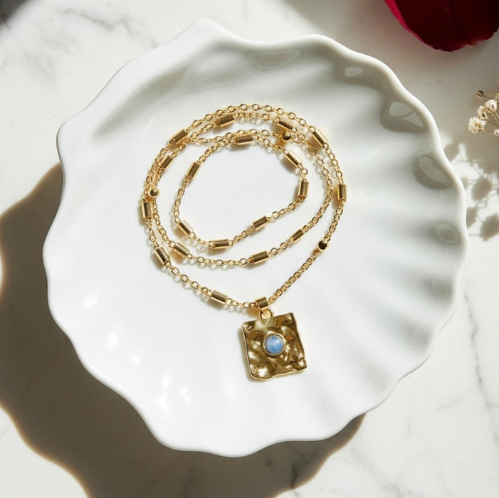 Gold necklace with a pendant on a white ceramic dish