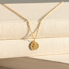 Gold necklace with a round pendant on a beige fabric background