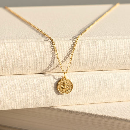 Gold necklace with a round pendant on a beige fabric background