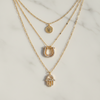 Three gold necklaces with different pendants on a light background