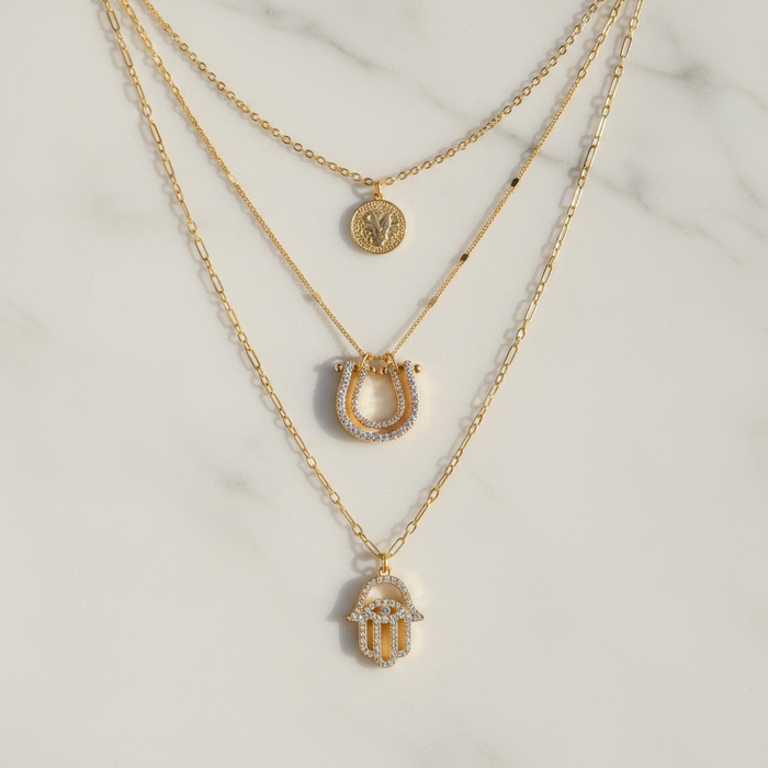Three gold necklaces with different pendants on a light background
