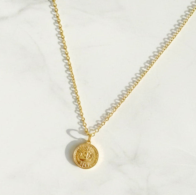 Gold necklace with a round pendant on a white background