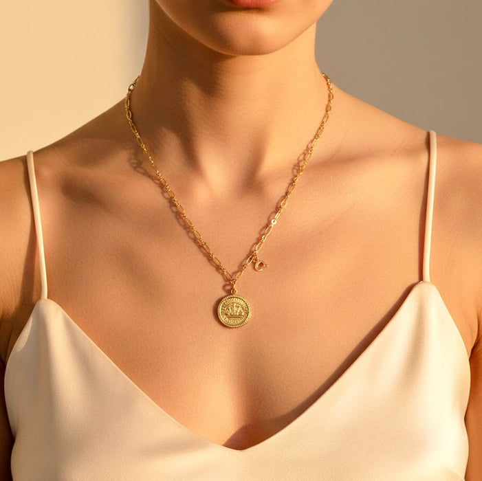 Gold necklace with a circular pendant worn by a person in a beige top.