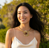 Woman wearing a gold necklace outdoors with greenery in the background