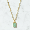 Gold necklace with a green pendant on a white marble background