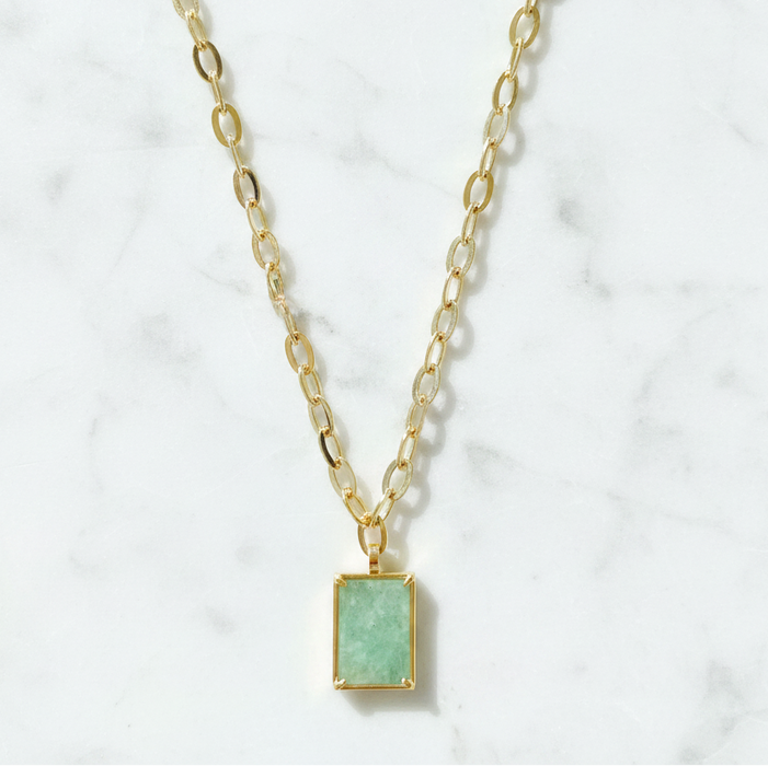 Gold necklace with a green pendant on a white marble background
