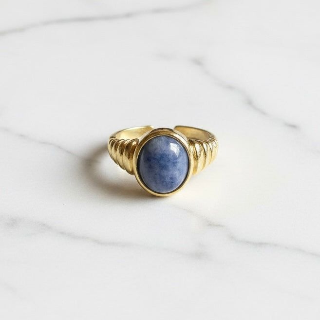 Gold ring with a blue stone on a marble surface