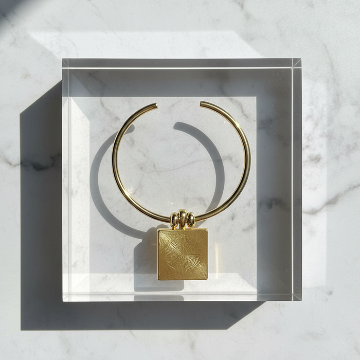 Gold necklace with a square pendant on a marble surface