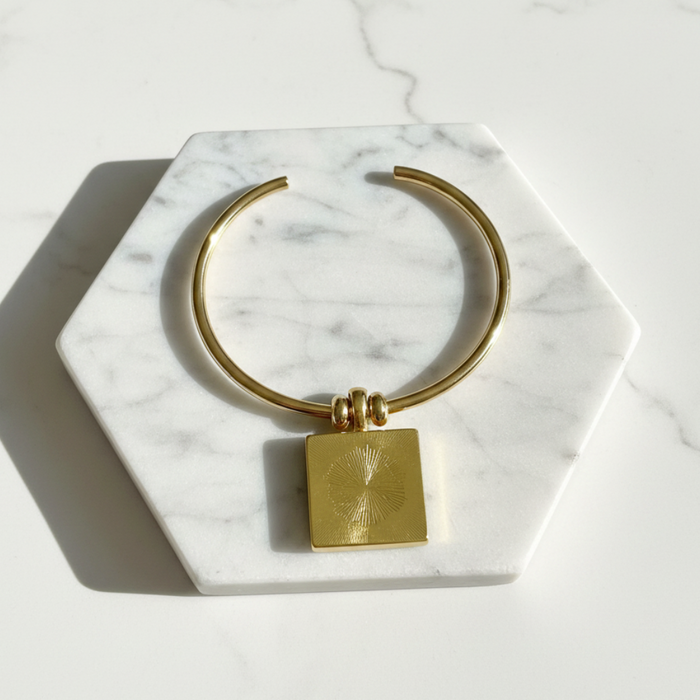 Gold bracelet with a square tag on a marble hexagonal coaster
