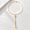 A gold chain necklace with a teardrop-shaped yellow gemstone pendant, accented by clear stones, displayed on a white marble surface.