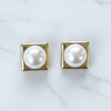 Pair of pearl earrings with gold square settings on a marble background