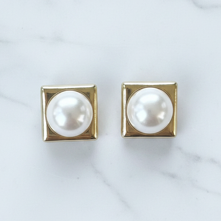 Pair of pearl earrings with gold square settings on a marble background