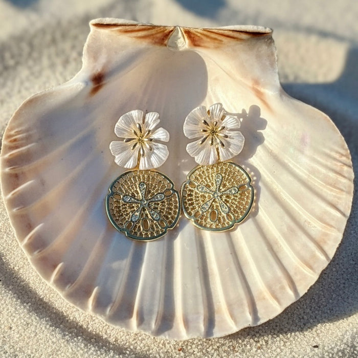 Pair of gold and silver floral earrings on a seashell with sand background