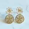 Pair of gold and white floral earrings on a light blue background