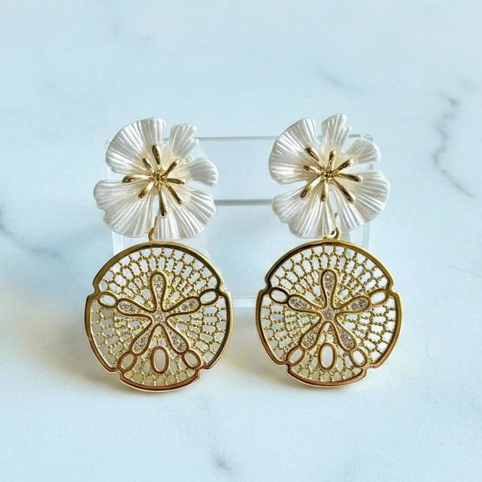 Pair of gold and white floral earrings on a light blue background