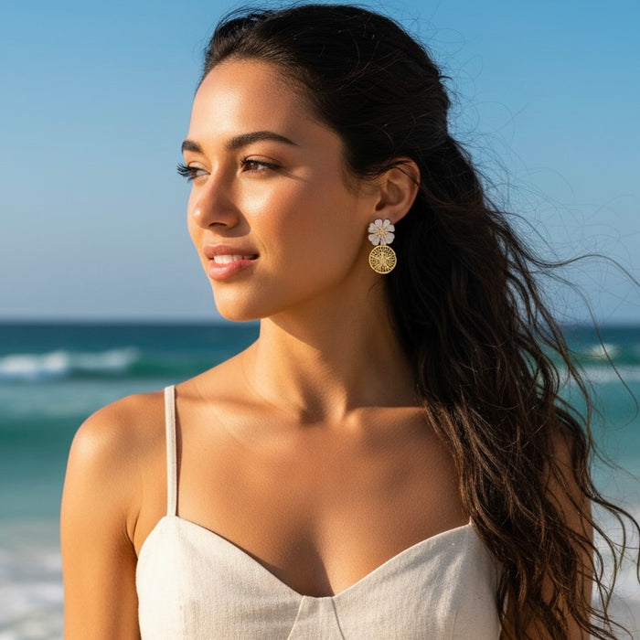 Woman on a beach wearing a light-colored dress with earrings, with ocean and sky in the background.