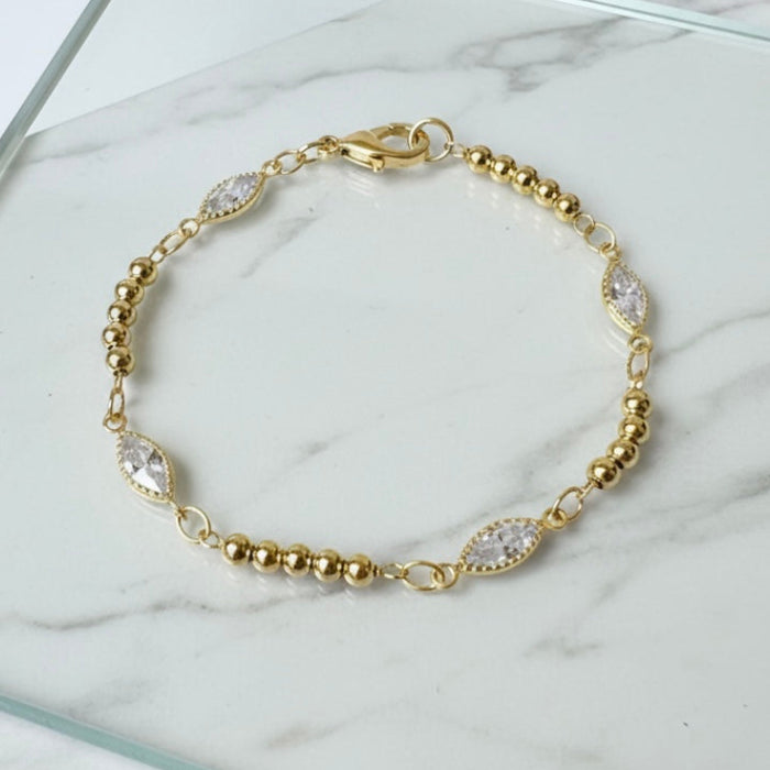 Gold bracelet with clear stones on a marble surface