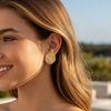 Woman wearing gold earrings with a blurred outdoor background