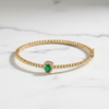 Gold bracelet with a green gemstone on a marble surface
